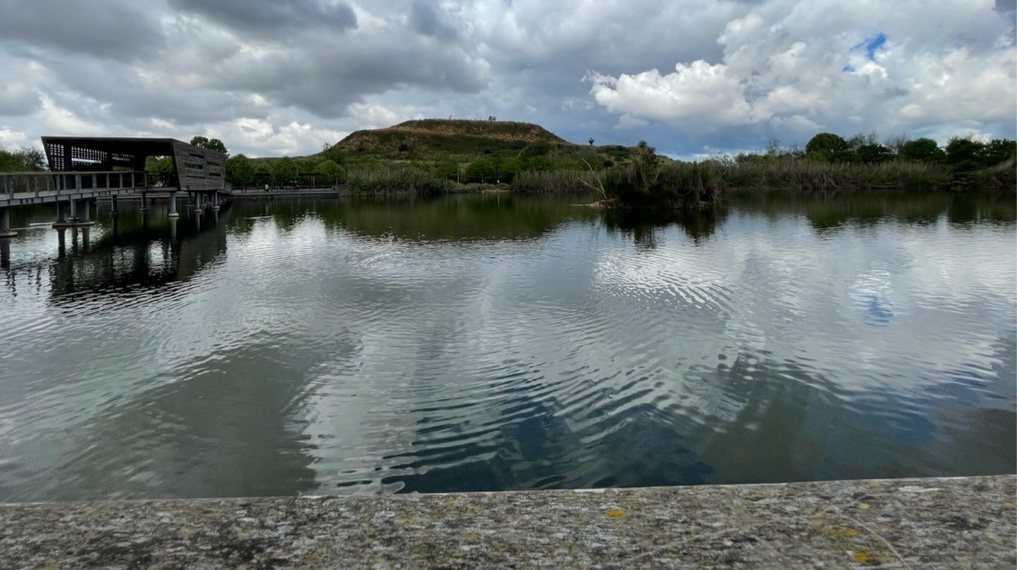 מראה מהשביל המעגלי בחלקו הצפוני - האגם בפארק האקולוגי בהוד השרון, הגשר החוצה אותו, הפרגולה במרכזו והר הזבל בולט מדרום